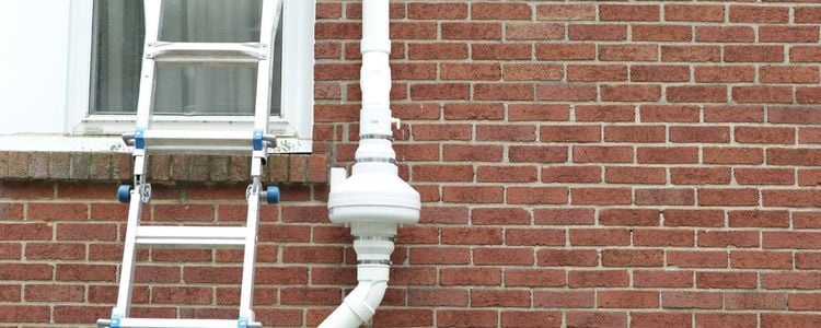 radon mitigation system on red brick wall with a ladder leaning against the wall next to it by a window